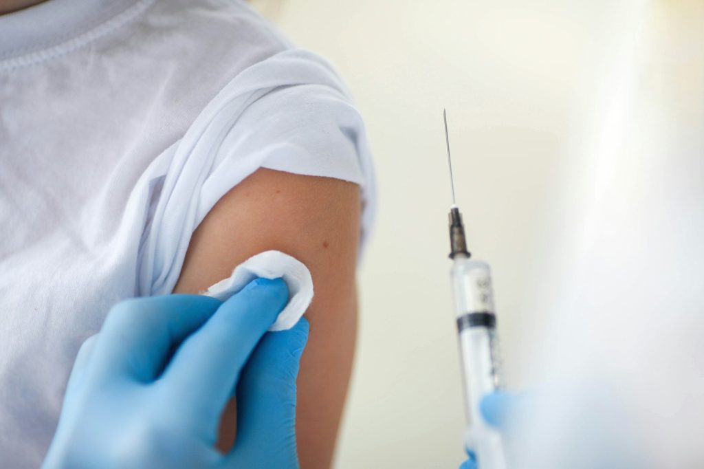child is shoulder and the hands of a doctor in medical gloves with an injection for vaccination.